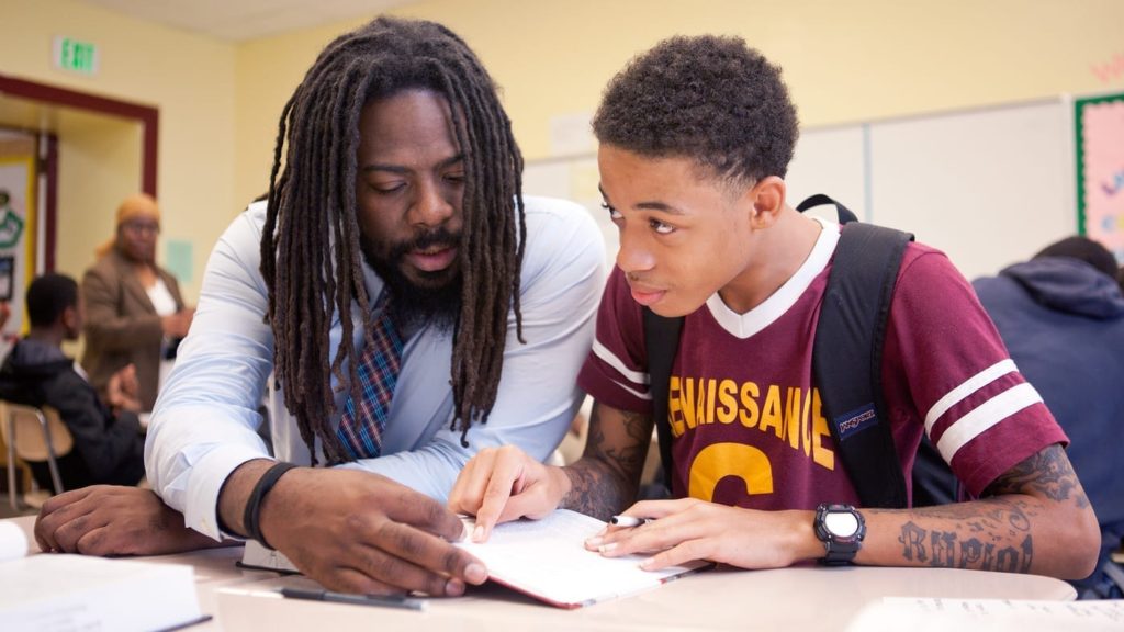 Mentor helps Black youth with schoolwork. 